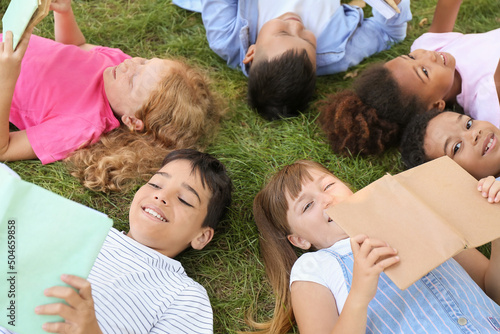 Little children with books lying on green grass in park