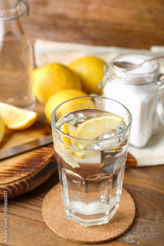 Glass of water with baking soda and lemon on wooden table