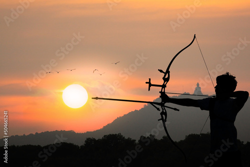 Silhouette of a man with  weapon bow and arrow on a background of sky and sunset