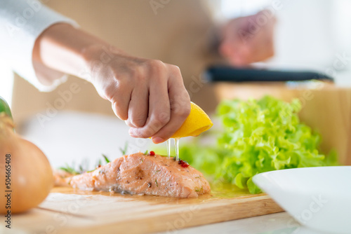 Fotografie Close up of Asian woman hand squeeze lemon juice on piece of salmon steak in the kitchen for dinner at home