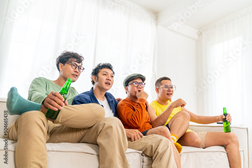 Group of Asian man friends sitting on sofa watching soccer game competition on television with drinking beer together at home. Happy male soccer fans cheering victory football team victory sport match © CandyRetriever 