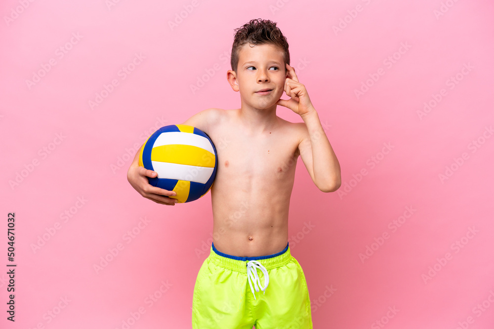 Little caucasian boy playing volleyball isolated on pink background having doubts and with confuse face expression