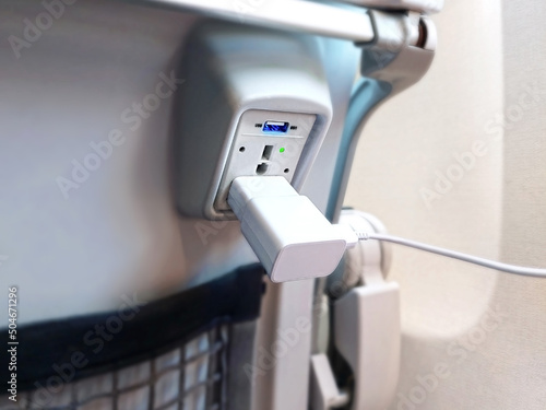 Close up of a USB and 110V power port plug on airplane seat for charging personal electronic batteries while flying. Devices such as phones, tablets, and laptops can be used for work and entertainment