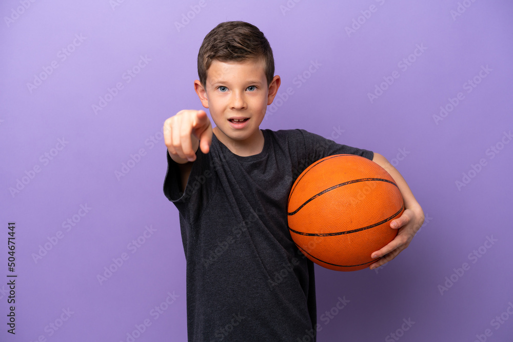 Little boy playing basketball isolated on purple background surprised and pointing front Little boy playing basketball isolated on purple background surprised and pointing front