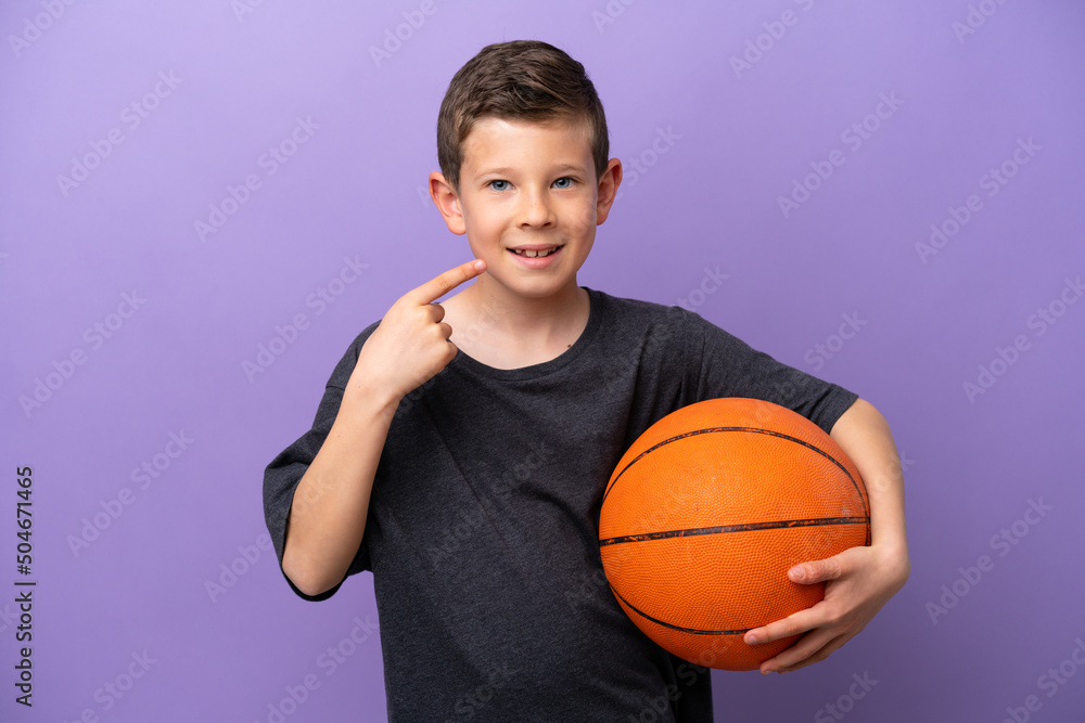 Little boy playing basketball isolated on purple background giving a thumbs up gesture