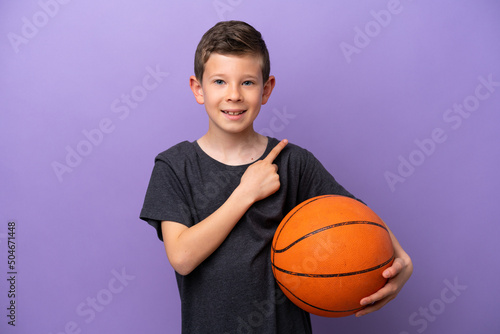 Little boy playing basketball isolated on purple background pointing to the side to present a product