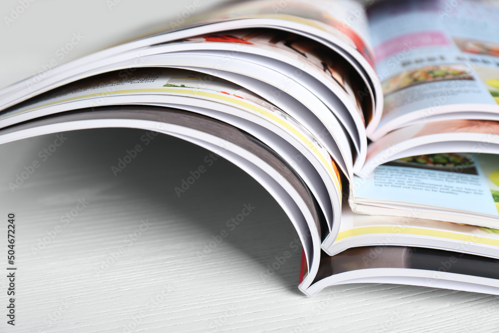 Many open magazines on white wooden table, closeup Many open magazines on white wooden table, closeup