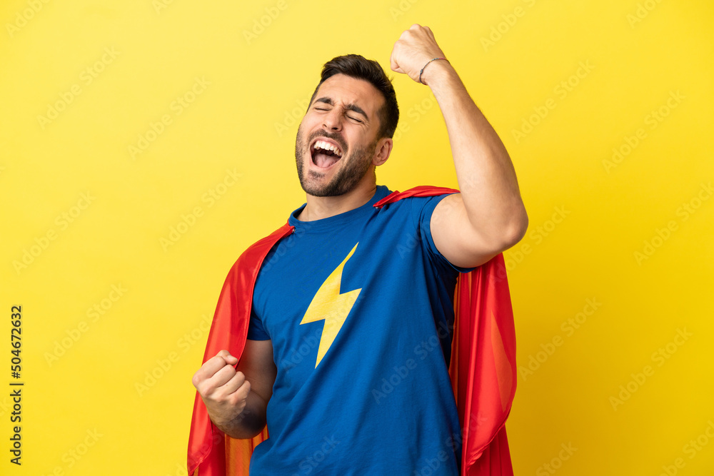 Young handsome caucasian man isolated on yellow background in superhero costume and celebrating a victory