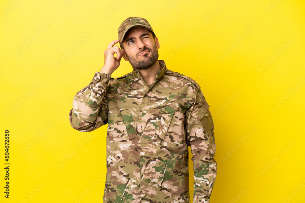 Military man isolated on yellow background having doubts and with confuse face expression Military man isolated on yellow background having doubts and with confuse face expression