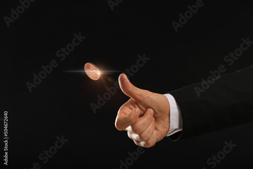 Man throwing coin on black background, closeup. Making decision photo
