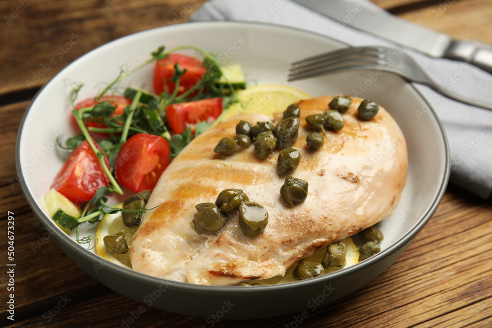 Delicious cooked chicken fillet with capers and salad served on wooden table, closeup Delicious cooked chicken fillet with capers and salad served on wooden table, closeup