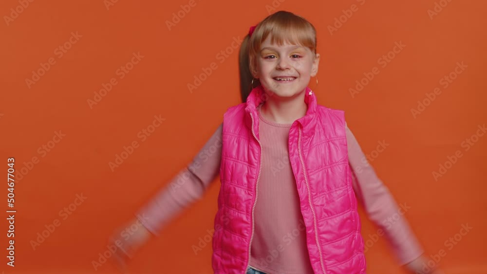 Funny joyful sincere little girl 6 years old in vest making playful silly facial expressions and grimacing, fooling around showing tongue. Young toddler child isolated alone on orange wall background Funny joyful sincere little girl 6 years old in vest making playful silly facial expressions and grimacing, fooling around showing tongue. Young toddler child isolated alone on orange wall background