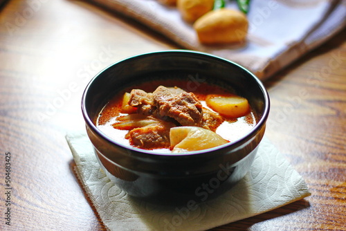 Massaman curry in black crockery served with boiled potatoes and chili on a brown wooden table. photo