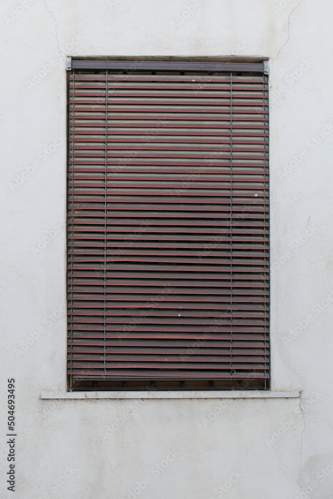 window with shutters, brown jalousie rolled up, grey cement wall, no person