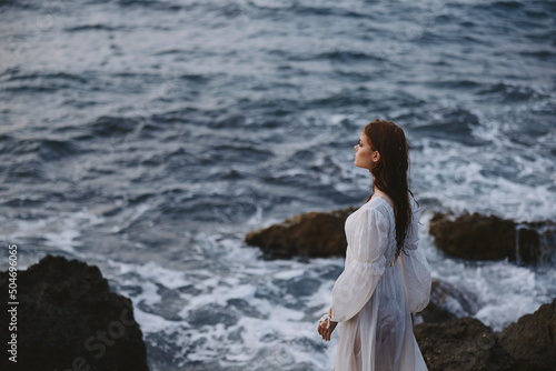 beautiful woman in a white wedding dress stands on the stones on the rocky coast of the ocean unaltered