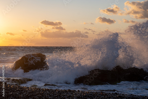 Sea ​​wave at sunset hitting rock on the beach.
