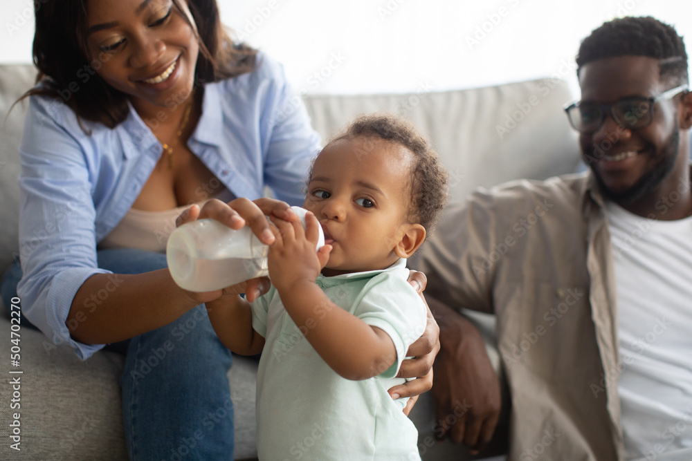 Young African American parents feeding child from bottle Young African American parents feeding child from bottle