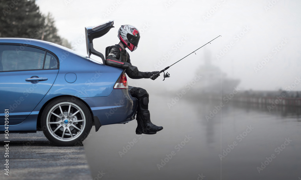Fishing from the car. A motorcyclist in full gear is fishing from the trunk  of a car Stock Photo