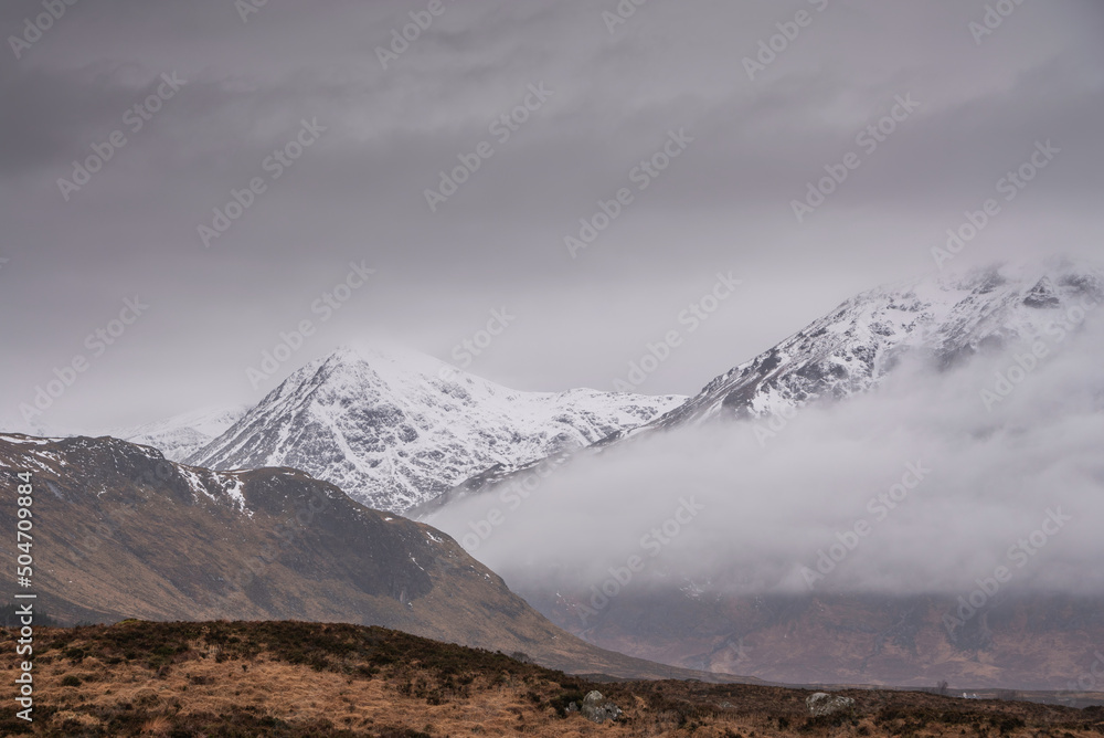 Beautiful Winter landscape of Buachaille Etive Mor Stob Dearg in Scottish Highlands engulfed in low cloud with snowcapped peaks