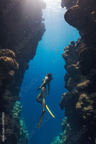 Woman freediver posing over sandy bottom with yellow fins. Freediving in blue ocean at Blue Hole Bells. Freediver young girl with fins glides undersea with sun rays. Snorkeling lovely asian girl swim photo