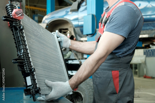 In the hands of an auto mechanic, an automobile radiator. Inspection and control of compliance, integrity of the spare part. Repair and maintenance in the car center.