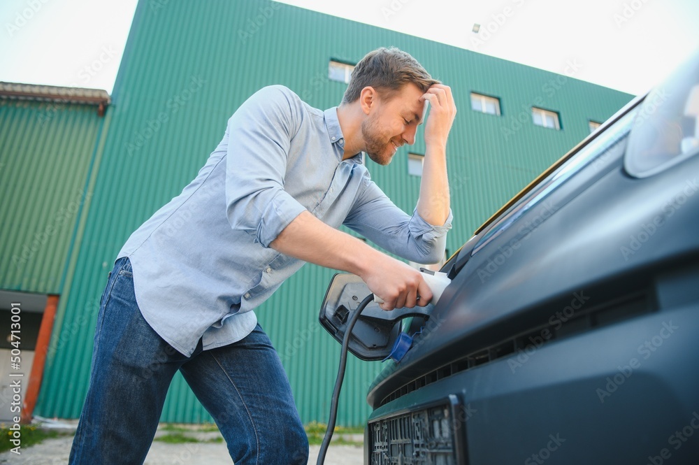 Smiling man unplugging the charger from the car Smiling man unplugging the charger from the car