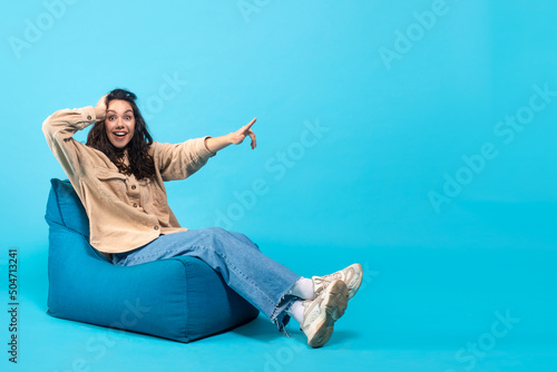 Glad surprised young european brunette lady with open mouth presses her hand to head sits on bagchair photo