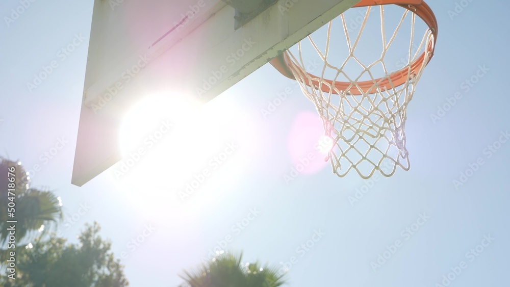 Orange hoop, net and backboard for basket ball game outside, basketball court outdoors. Recreational sport equipment on streetball field or playground. Blue sky and beach palm trees, California USA.