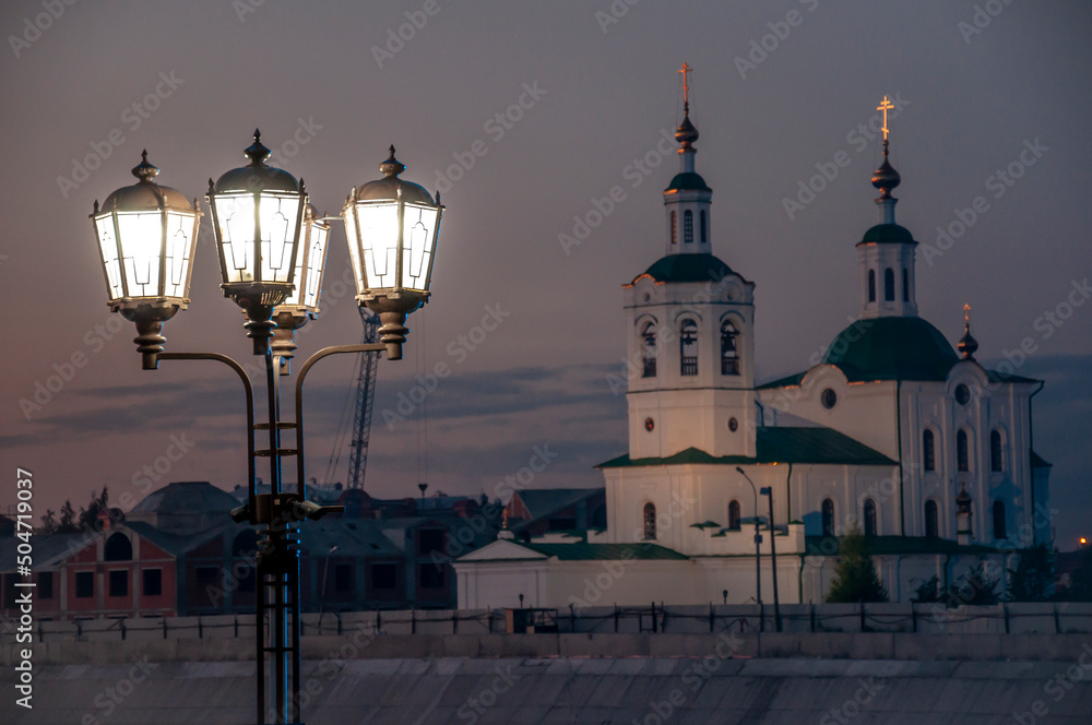 Street lights are located on the streets of the city on the background with a church. Street lights are illuminating everything around the black night