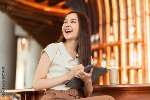 asian female freelancer digital nomad hand using tablet working remotely anywhere workation sit at counter near coffee makeing bar contact abroad client with cheerful smiling peacefel success deal photo