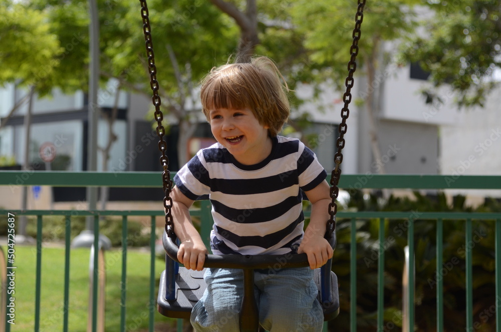 happy little boy playing on playing on the playground at the day time European boy on chain swing. happy little boy playing on playing on the playground at the day time European boy on chain swing.