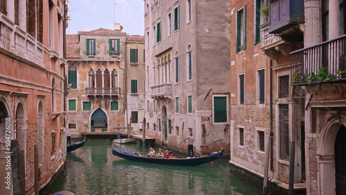 Gondola go down canal at day, Venice, Italy. Gondolier navigate boat. Tourists enjoy ride and take photos. Medieval buildings, channel waters 