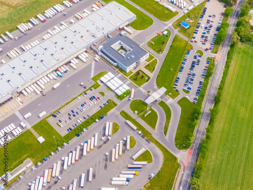 Aerial view of a logistics park with warehouse, loading hub and many semi trucks with cargo trailers standing at the ramps for load/unload