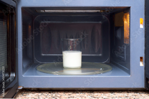 Half-filled glass of milk in a blue microwave, ready to be heated.