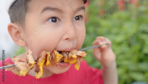 Hungry boy biting chicken BBQ from skewer.  photo