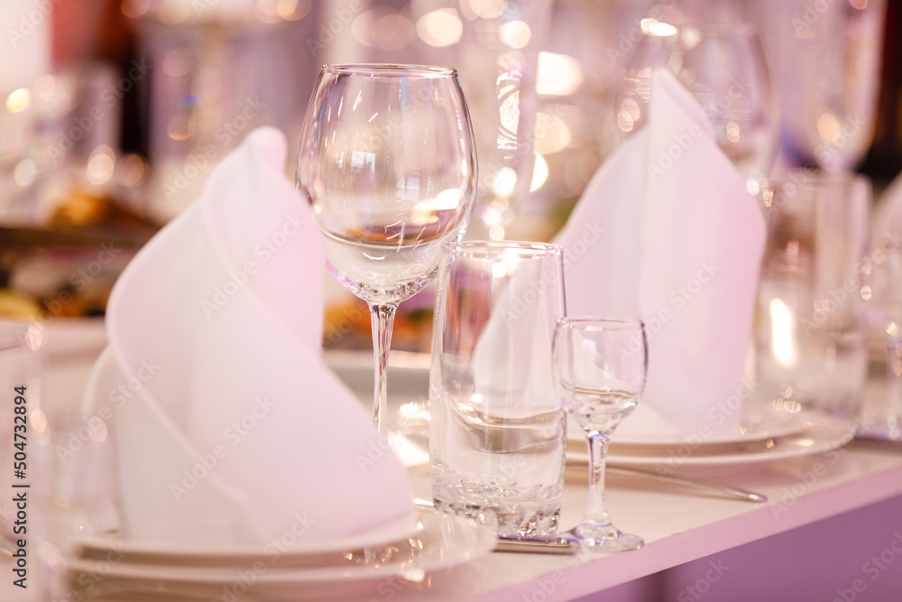 Empty glass set in restaurant. wedding, decor, celebration, holiday concept - romantic table setting with white tablecloth, plates, crystal glasses