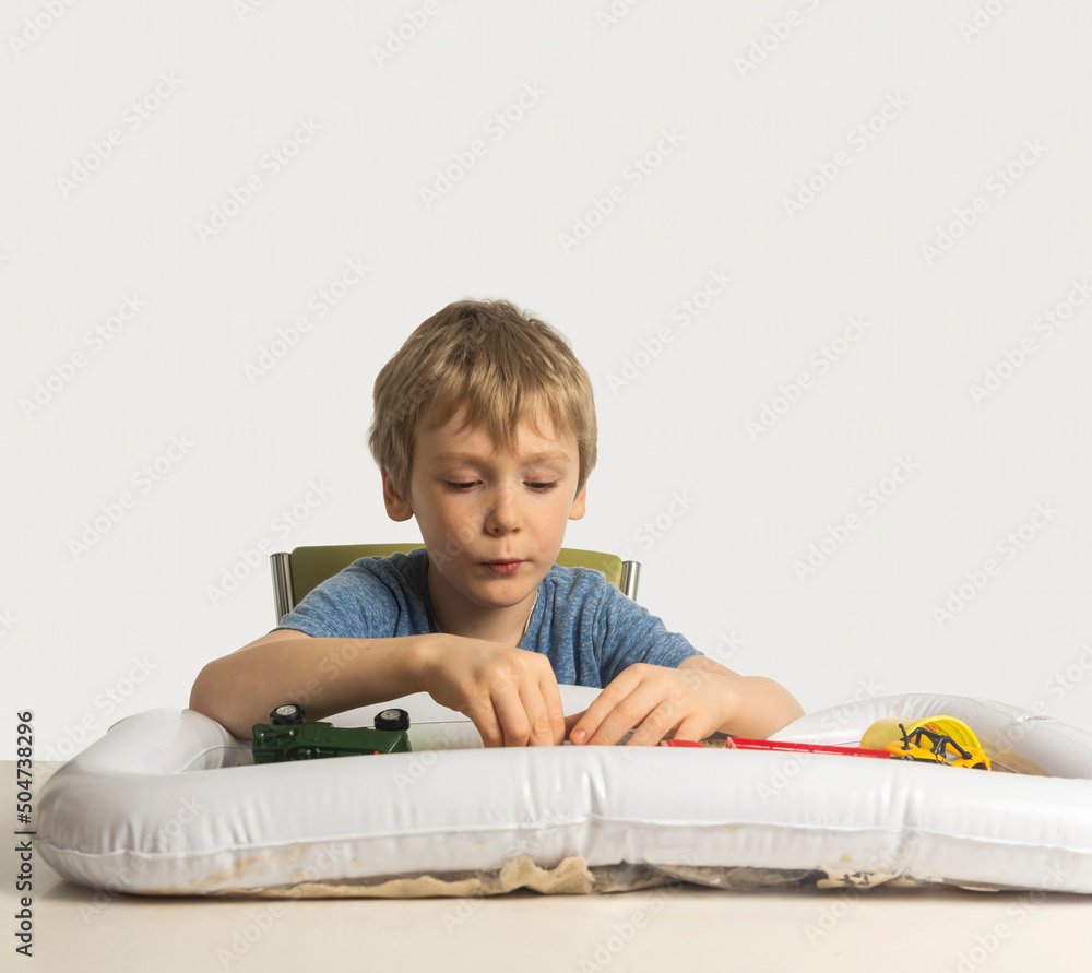 a boy with blond hair plays with sand in an inflatable sandbox for the house. a boy with blond hair plays with sand in an inflatable sandbox for the house.