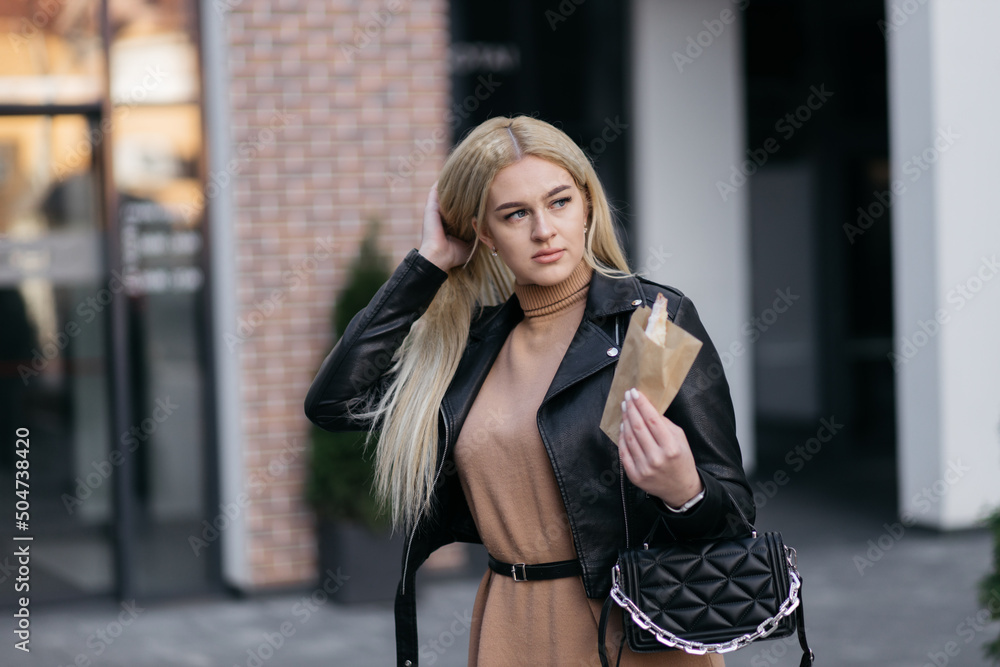 Blonde girl holding a package of croissants on the background of the mall. Beautiful girl in the city center. Croissant in a package.