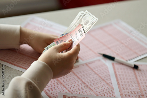 A young woman holds the lottery ticket with complete row of numbers and dollar bills on the lottery blank sheets background photo