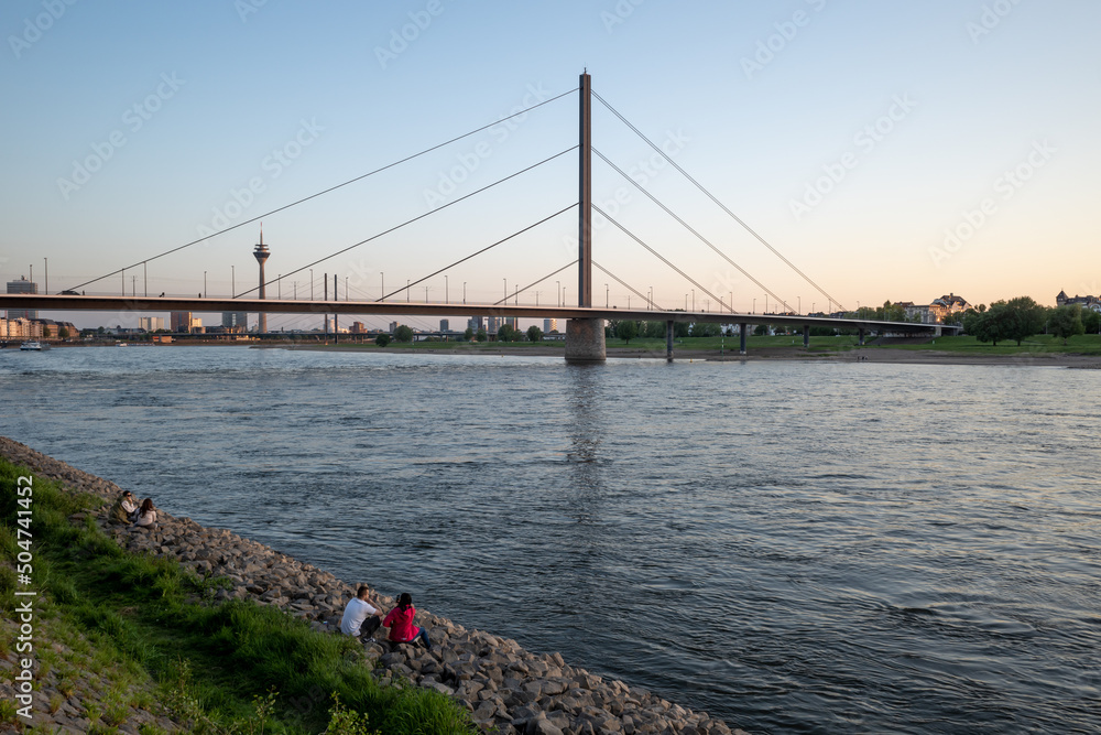 Naklejka premium Outdoor scenery of people sit and enjoy nice atmosphere at promenade along riverside of Rhine River during evening sunset time in Düsseldorf, Germany.