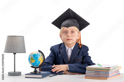 Straight-A student sits at table next to notebooks, textbook and globe. Schoolboy in school uniform and student hat.