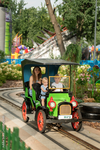 Amusement park. Young mother and two children ride in small car. Nanny rides with children in the park. © somemeans
