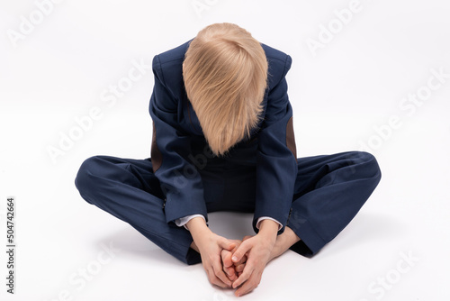 Boy in school uniform sits with head down and hands on his legs. Tired or sad blond schoolboy. © somemeans
