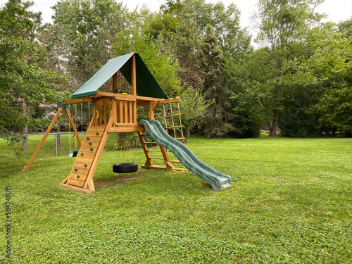  wood backyard playset with wave slide, two clubhouses, rock climbing wall, swings with tire swing, an access ladder photo
