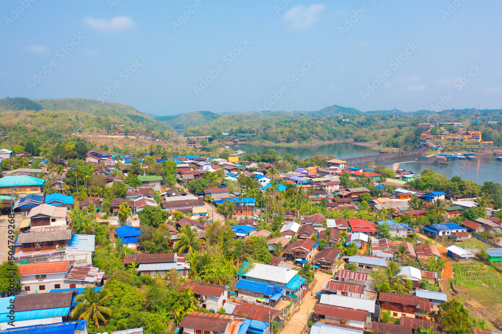 Aerial top view of residential local houses in Mon village, nature trees with lake or river, Kanchanaburi, Thailand in urban city town in Asia, buildings.