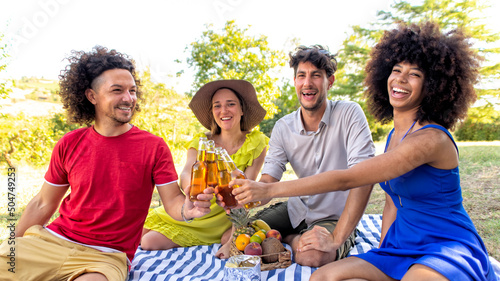 summer holidays outdoor picnic. multiracial group of friends having food and drinking beers laying on a blanket in a park garden. people happy hour enjoying together a break toast. lifestyle concept