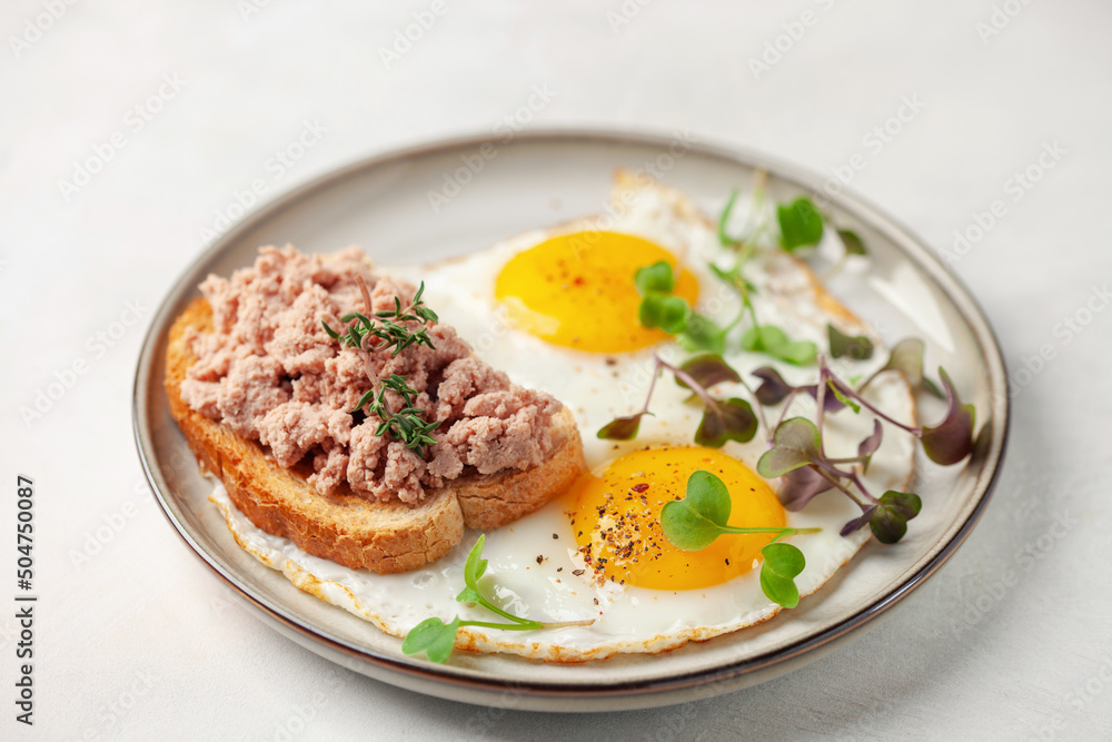 Breakfast - fried eggs and a sandwich with goose pate in a plate on the table Breakfast - fried eggs and a sandwich with goose pate in a plate on the table