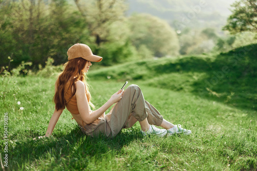 Bottom view young student freelancer woman in green jacket jeans sit on bench in spring park outdoors talk by mobile cell phone look aside. People urban lifestyle concept photo