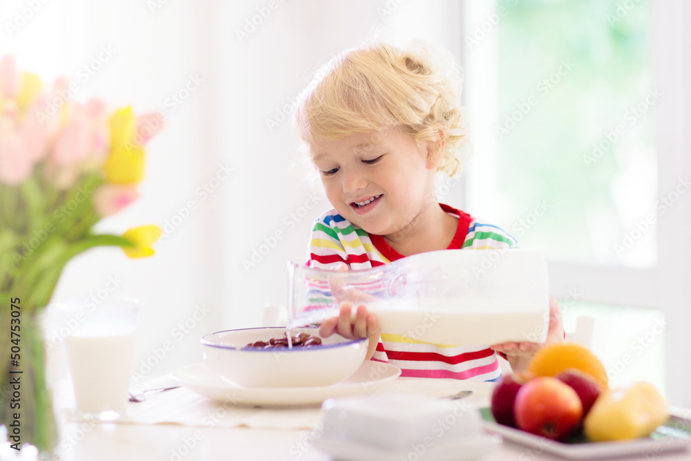 Child eating breakfast. Kid with milk and cereal.