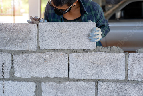 masonry worker make concrete wall by cement block and plaster at construction site